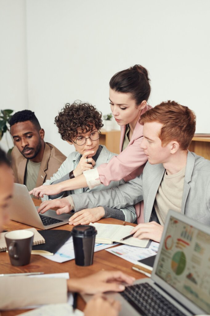 group of four mid-20s individuals gather at a computer, seemingly discussing the work they are collaborating on.
